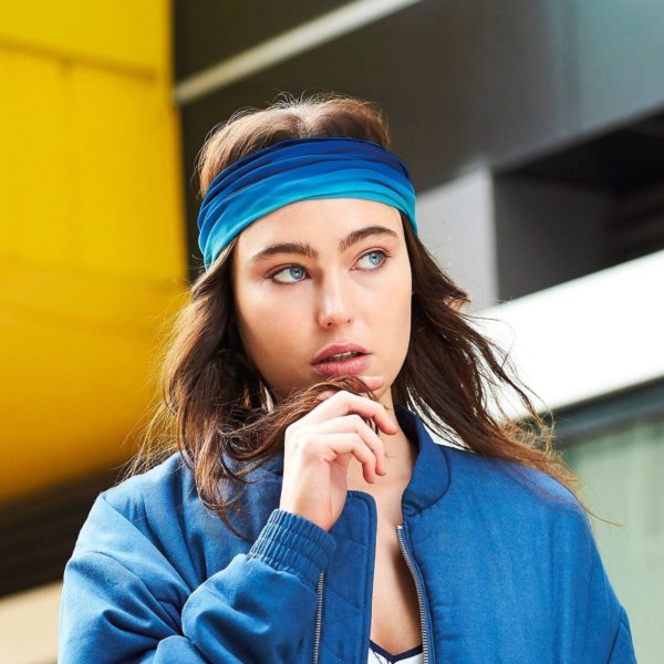 Ragazza con lunghi capelli castani e fascia in fronte blu, bomber blu aperto e sfondo case