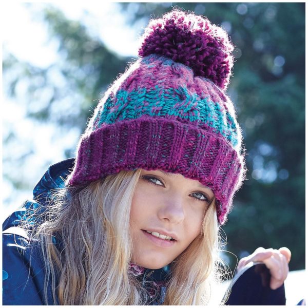 Ragazza bionda con berretto pon pon maglia in diversi filati colore winter berries con sfondo bosco