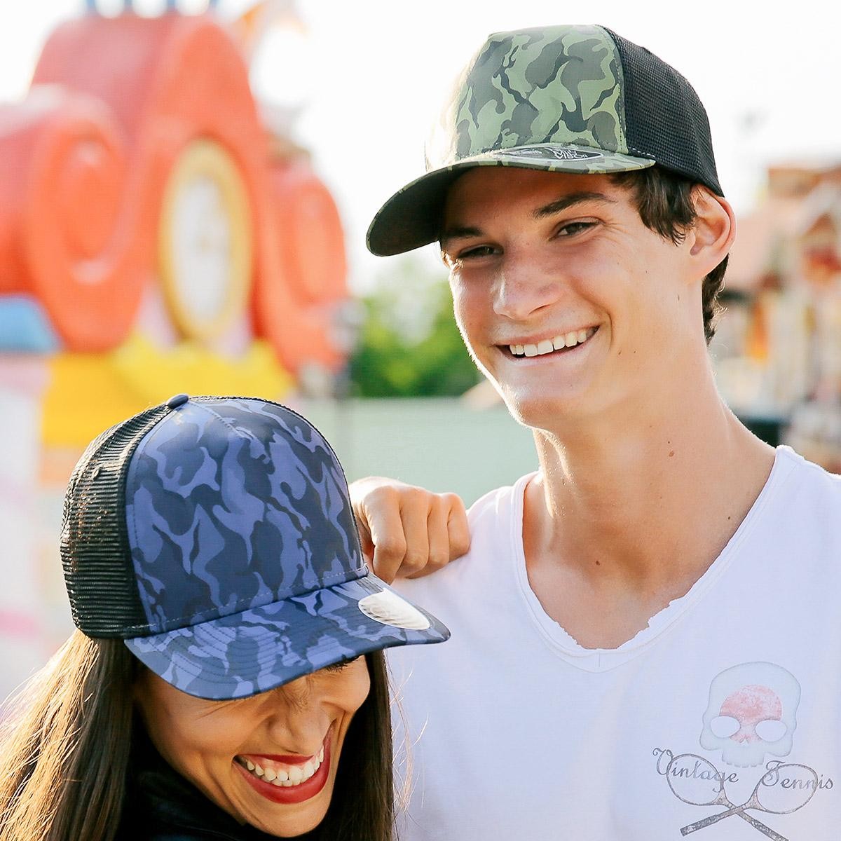 Ragazza con cappellino blu con braccio appoggiato su spalla di ragazzo con cappellino verde