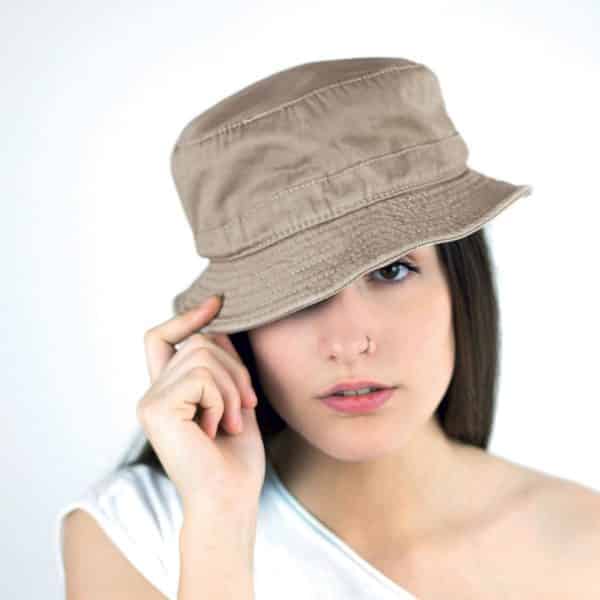 Ragazza con tshirt bianca, lunghi capelli castani e piercing indossa cappellino beige tenendo la falda