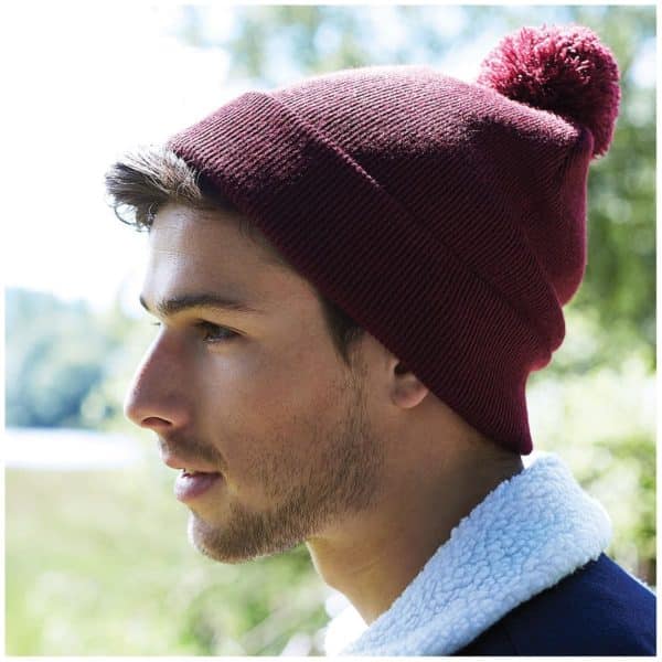 Primo piano di ragazzo in un bosco con berretto bordeaux a maglia con risvolto e pon pon
