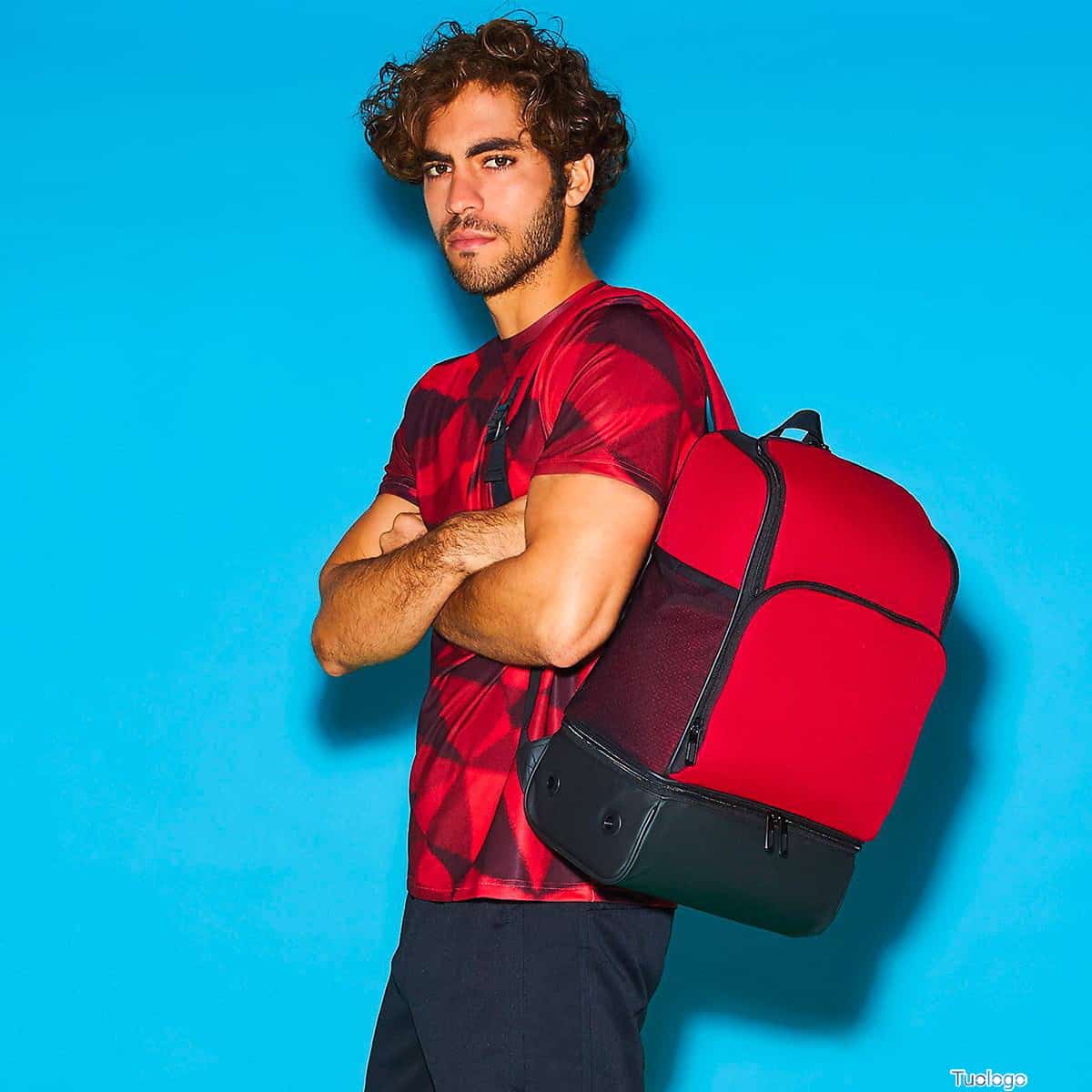 Ragazzo con capelli ricci e castani e abbigliamento sportivo con zaino rosso e nero su sfondo blu