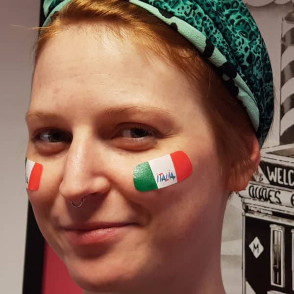 Ragazza in primo piano sorridente, con sticker sulle guance con la bandiera italiana per il tifo