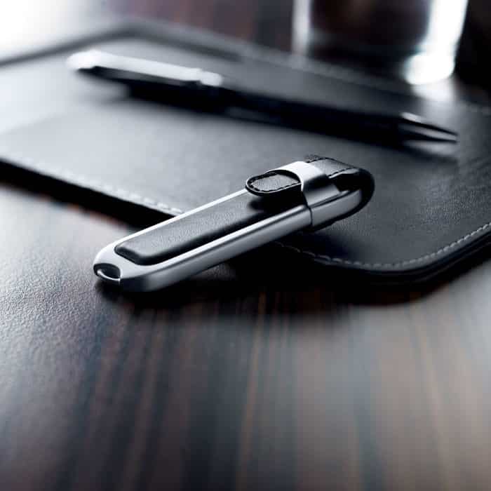 Chiavetta usb grigia in metallo con rifiniture in pelle nera su un tavolo