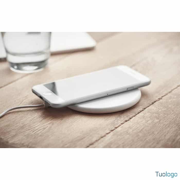 Smartphone sopra caricatore tondo bianco, sopra tavolo da lavoro in legno