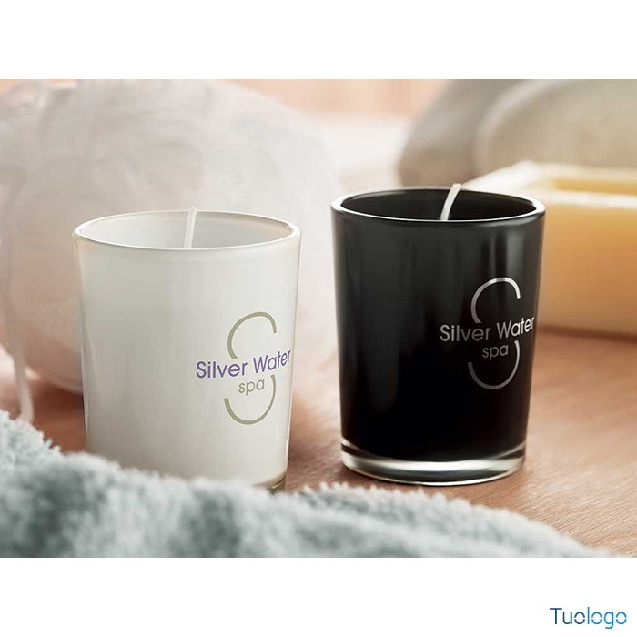 Due candele con logo, una bianca e una nera, dentro portacandele in vetro, su tavolo