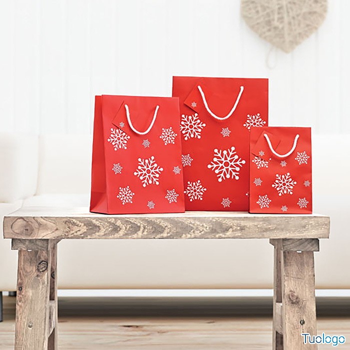 Tre shoppers rosse con fiocchi di neve bianchi sopra tavolo di legno