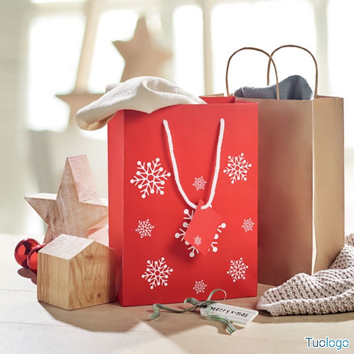 Due shopper, una rossa con motivo fiocchi di neve e una neutra color cartone, su tavolo con blocchi di legno a tema natalizio